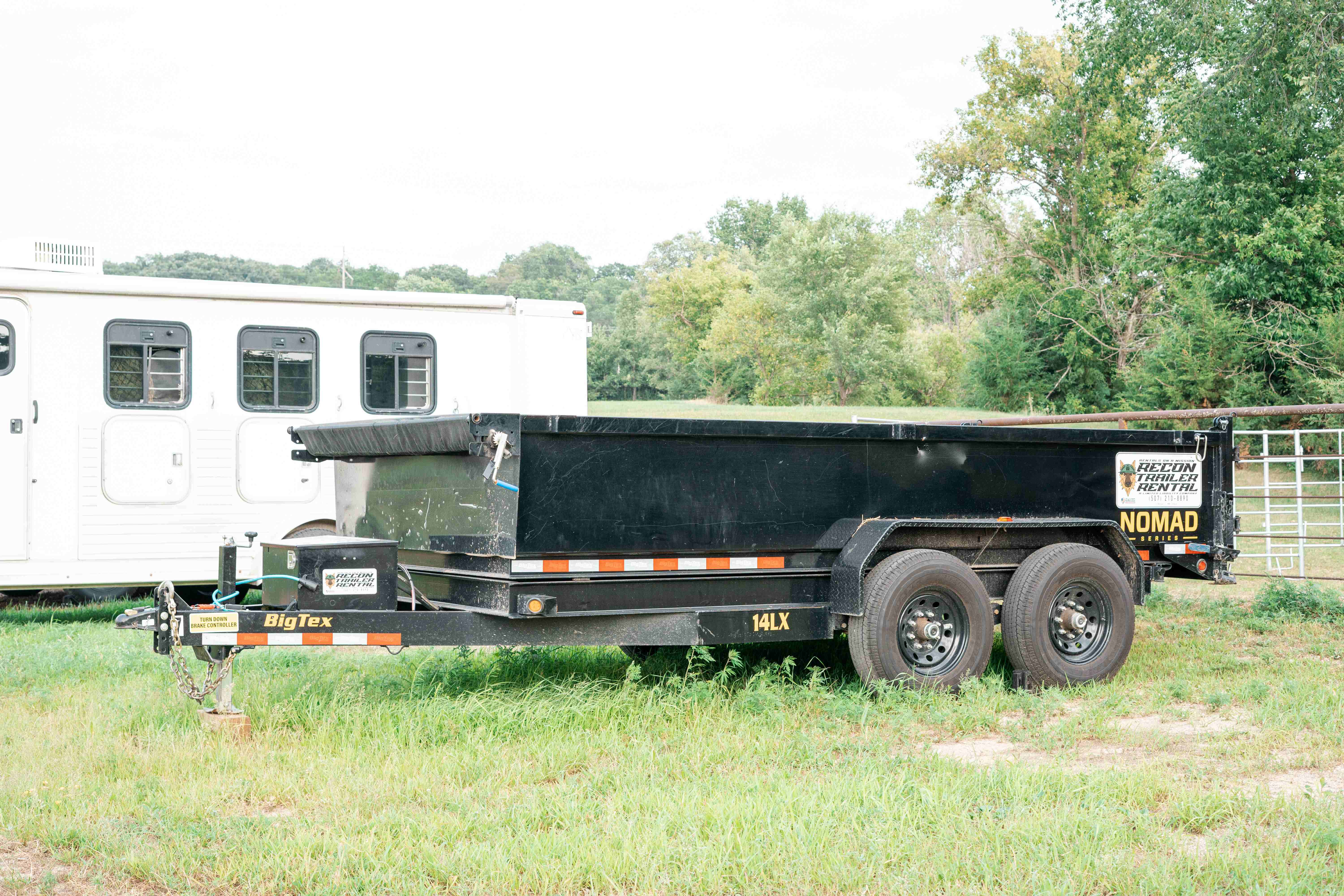 BigTex dump trailer side profile in grass field showing dual axle wheels