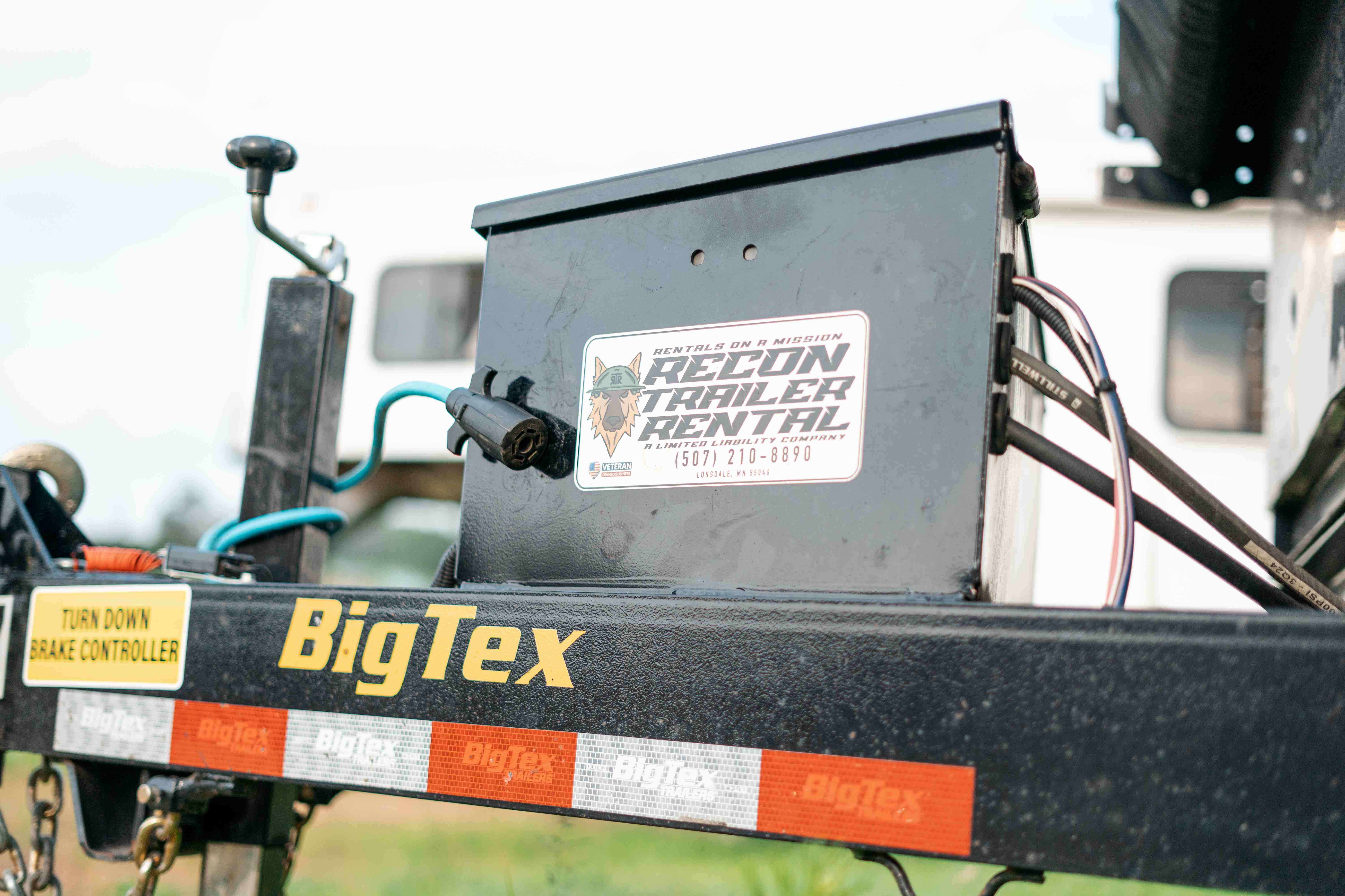 Close-up of BigTex dump trailer tongue toolbox with Recon Trailer Rental sticker and turn down brake controller label