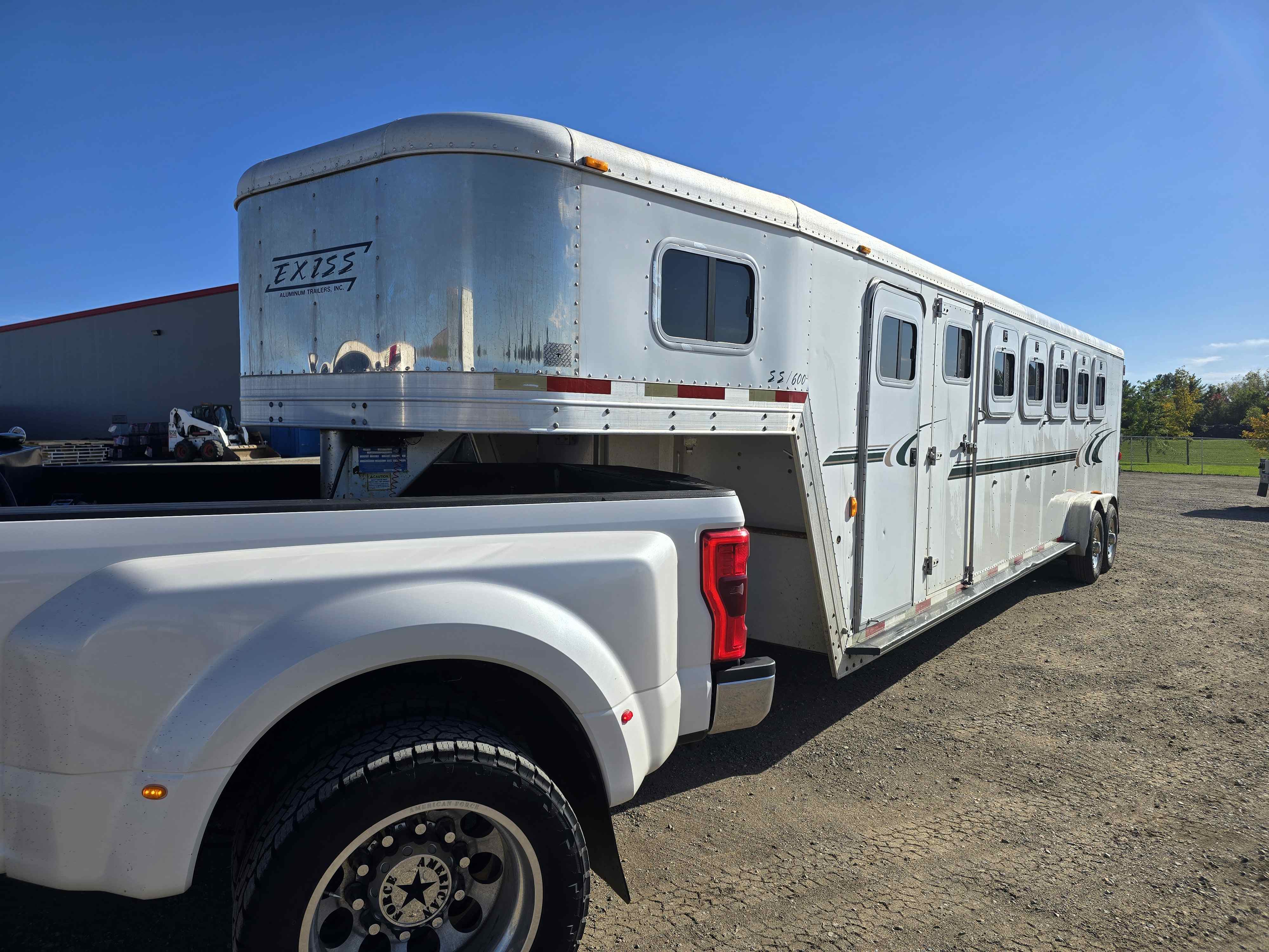 Exiss SS600 horse trailer rear-quarter view hitched to a white dually truck near a warehouse