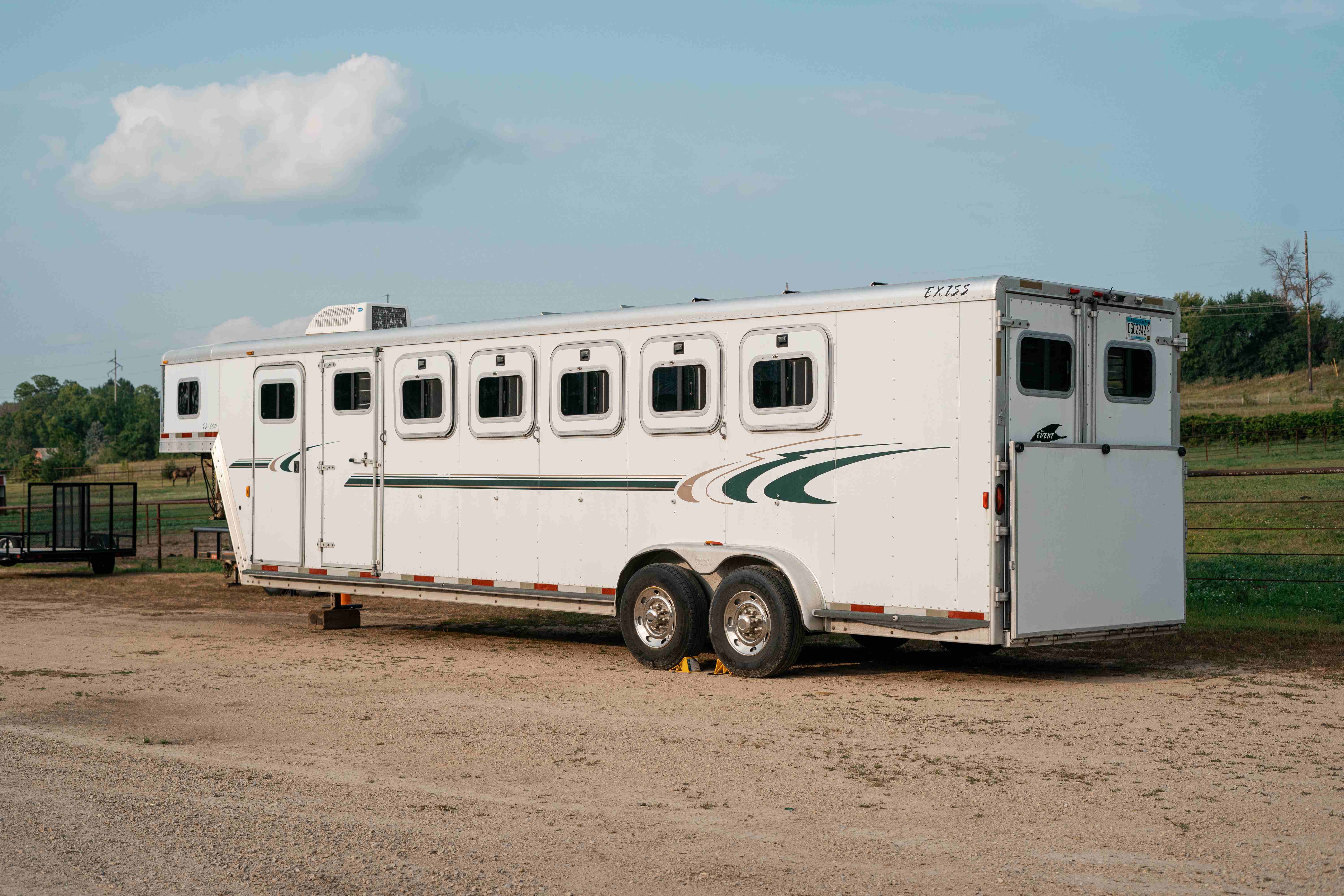 Exiss SS600 horse trailer side profile parked in a dirt lot with horses grazing in the background