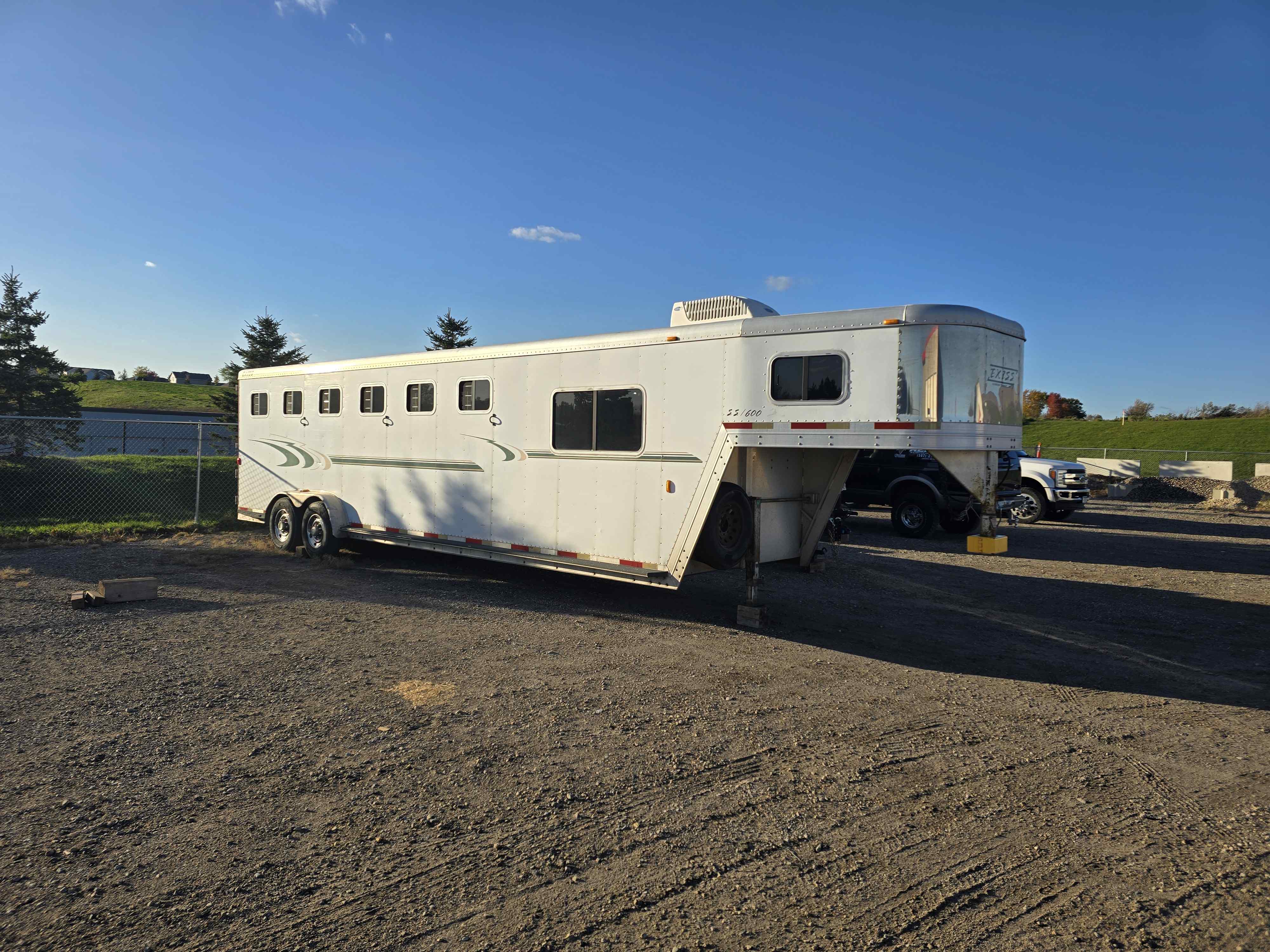 Exiss SS600 horse trailer rear-quarter view on a gravel lot with gooseneck raised