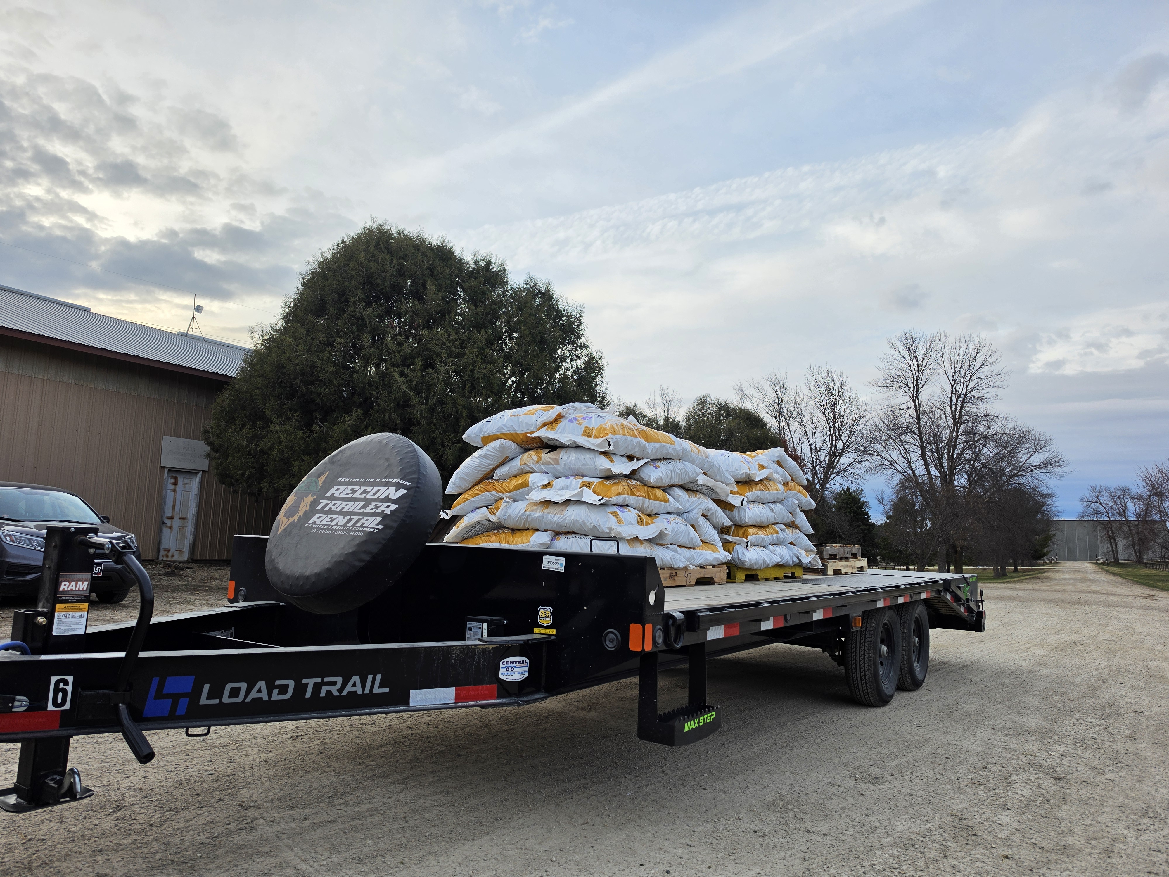 Load Trail deckover trailer loaded with bags of feed on pallets showing real-world hauling capacity with Recon Trailer Rental spare tire cover
