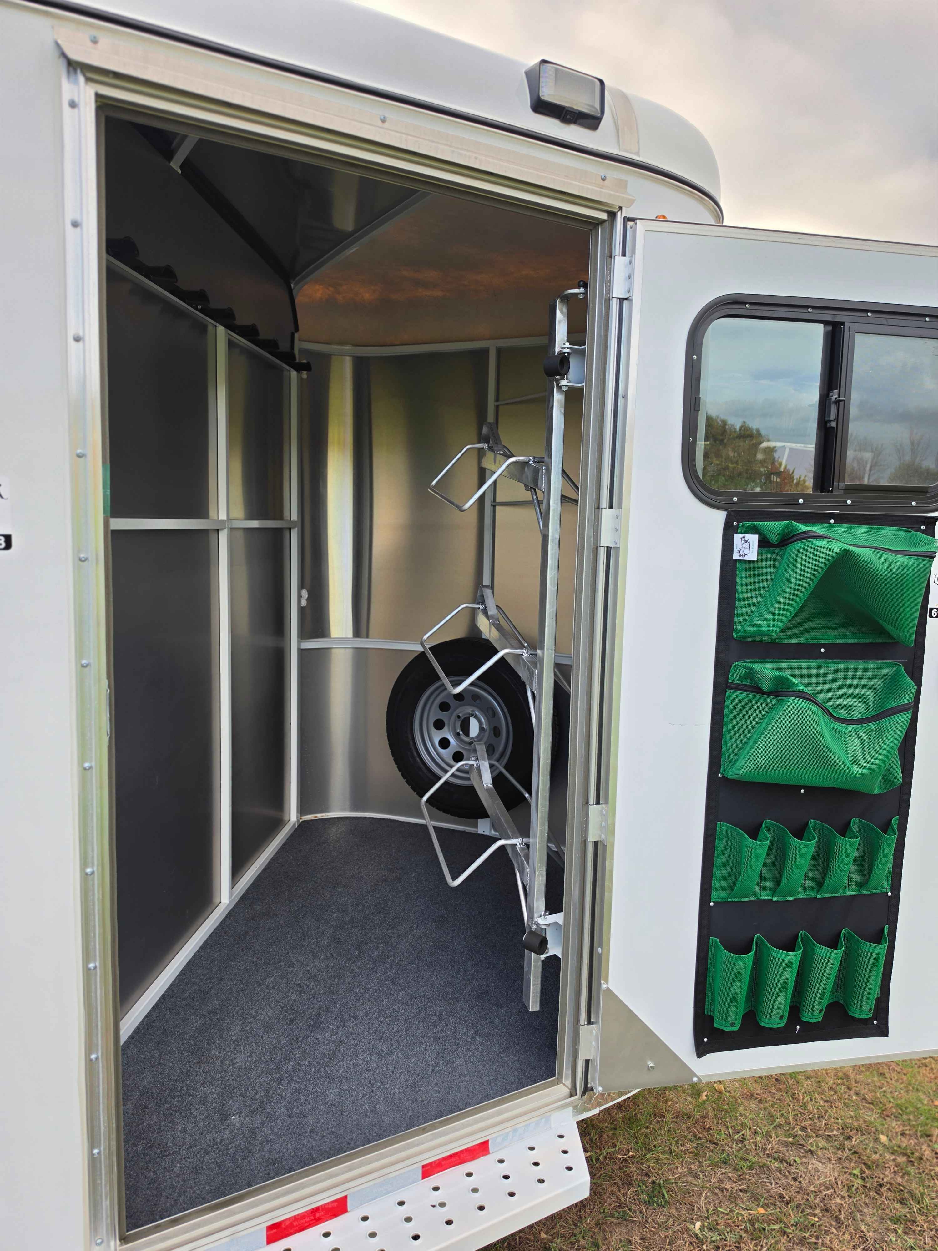 Front tack room of the 3 horse stock combo with saddle racks, spare tire mount, and green mesh gear pockets on the door
